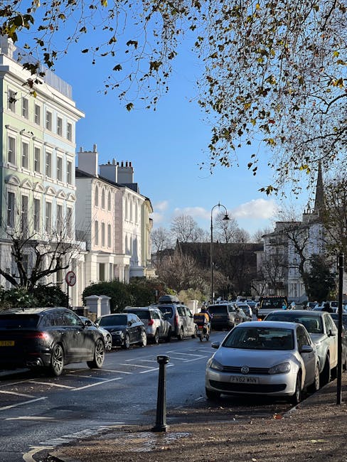 A narrow street in Putney, SW15, with parked cars lining both sides and pedestrians walking along the pavement. The buildings on the left feature colorful facades with retail shops and street-level aw